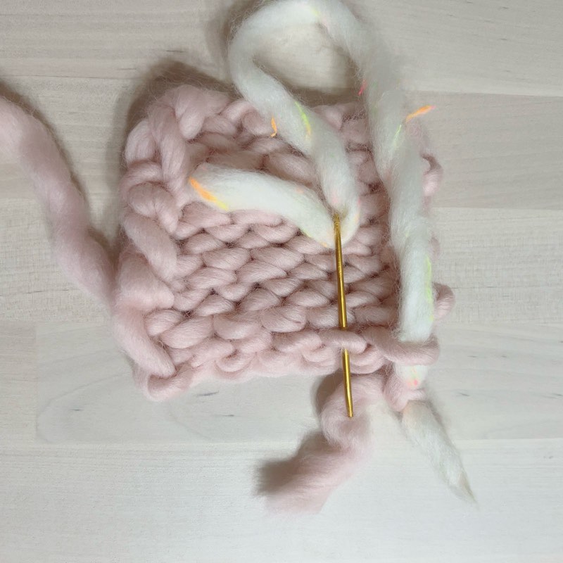 ピンクの毛糸と編み地　白い毛糸で糸始末　2つめ通すところ